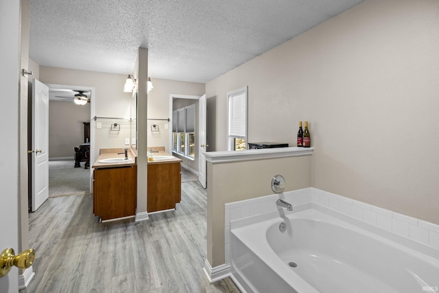 bathroom with a bathing tub, ceiling fan, a textured ceiling, wood-type flooring, and vanity