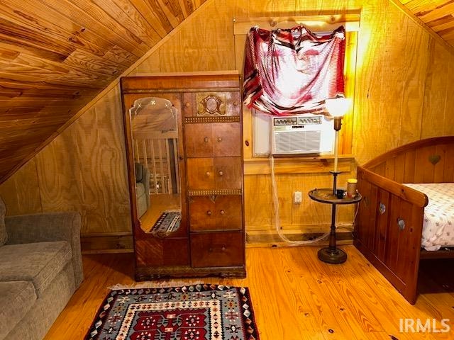 living area featuring cooling unit, wooden ceiling, light wood-type flooring, vaulted ceiling, and wooden walls