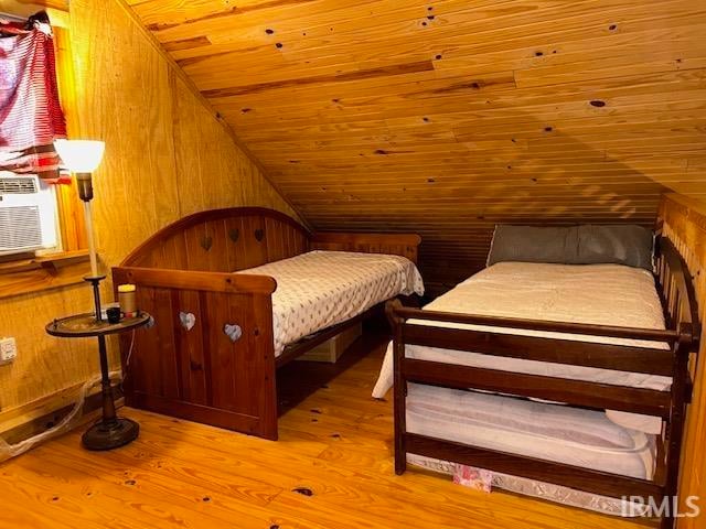 bedroom with light hardwood / wood-style floors, wooden ceiling, lofted ceiling, and wooden walls