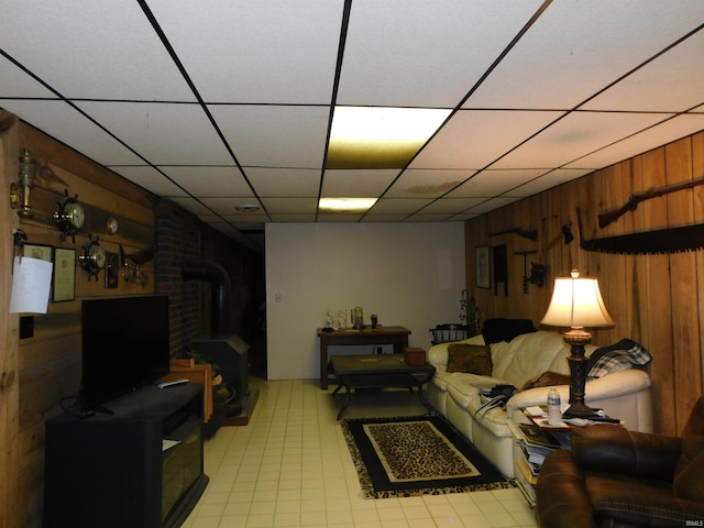 living room with wooden walls, a drop ceiling, and a wood stove