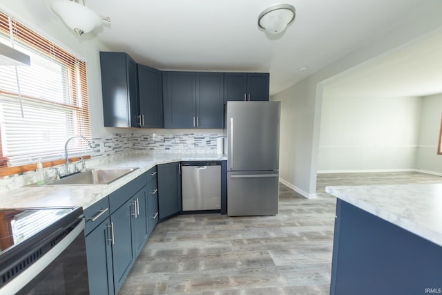 kitchen featuring light hardwood / wood-style flooring, backsplash, sink, blue cabinetry, and appliances with stainless steel finishes