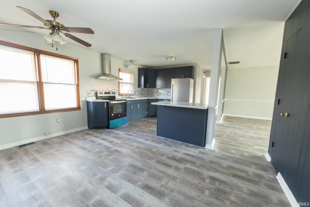 kitchen with wall chimney range hood, tasteful backsplash, ceiling fan, appliances with stainless steel finishes, and light hardwood / wood-style floors