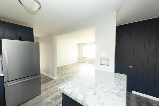 kitchen with a kitchen island, light stone countertops, stainless steel refrigerator, light hardwood / wood-style flooring, and wooden walls