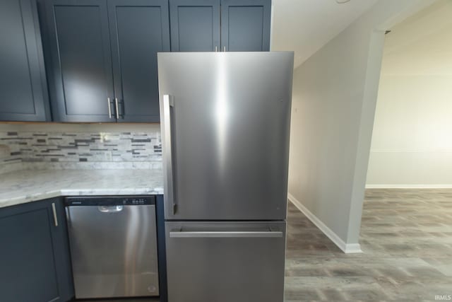 kitchen featuring light stone countertops, appliances with stainless steel finishes, backsplash, blue cabinets, and light hardwood / wood-style floors