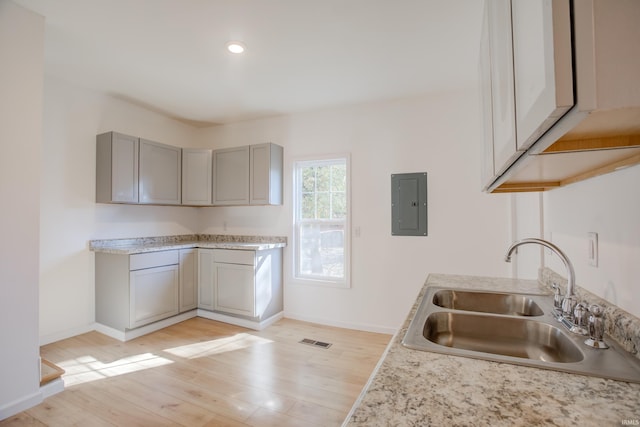 kitchen with gray cabinets, light hardwood / wood-style floors, sink, and electric panel