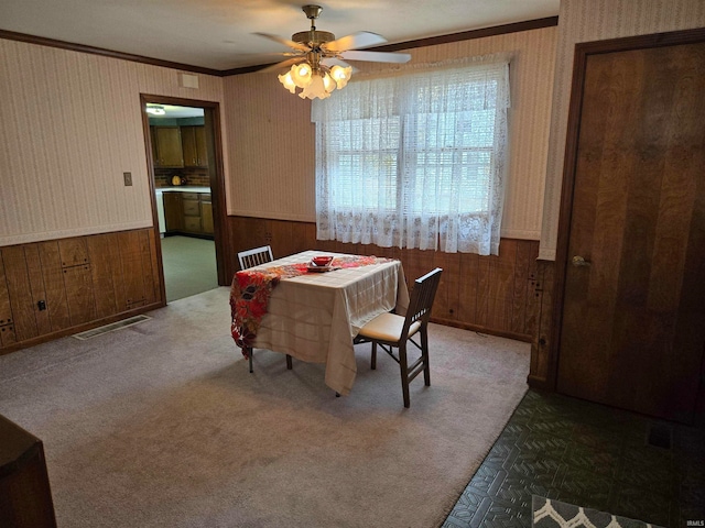 dining area featuring ceiling fan, ornamental molding, and wood walls