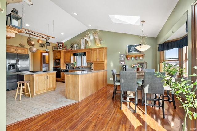 kitchen with black appliances, a skylight, a center island, light hardwood / wood-style floors, and high vaulted ceiling