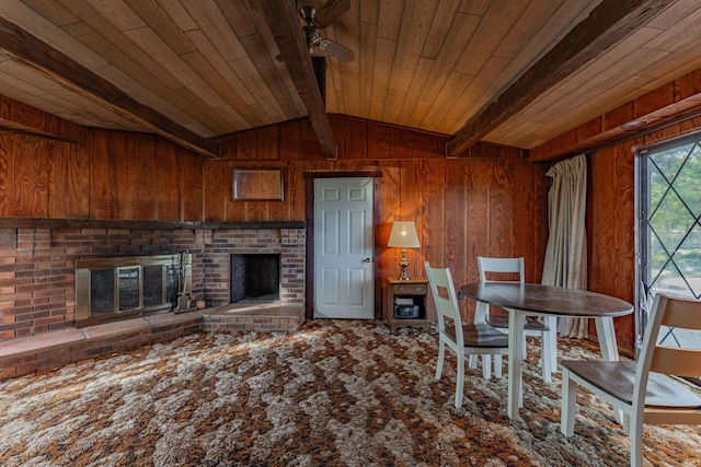 dining room featuring wooden walls, ceiling fan, a fireplace, vaulted ceiling with beams, and wood ceiling