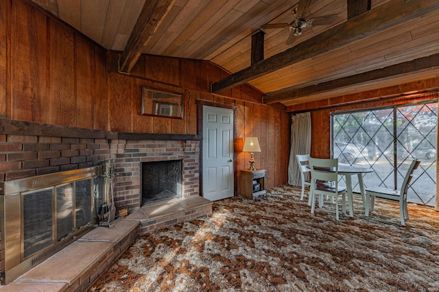 living area with wooden walls, a brick fireplace, a ceiling fan, wooden ceiling, and vaulted ceiling with beams