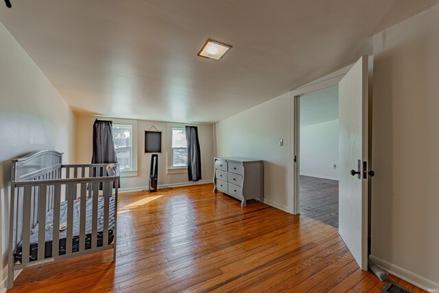 bedroom with lofted ceiling, a nursery area, and light wood-type flooring