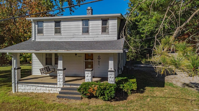 country-style home with a porch, roof with shingles, a front yard, and a chimney