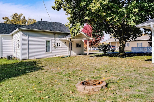 back of house featuring central AC, a lawn, and a fire pit