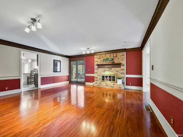 unfurnished living room with crown molding, a brick fireplace, hardwood / wood-style flooring, and french doors