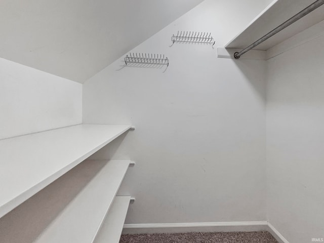 walk in closet with vaulted ceiling and dark colored carpet