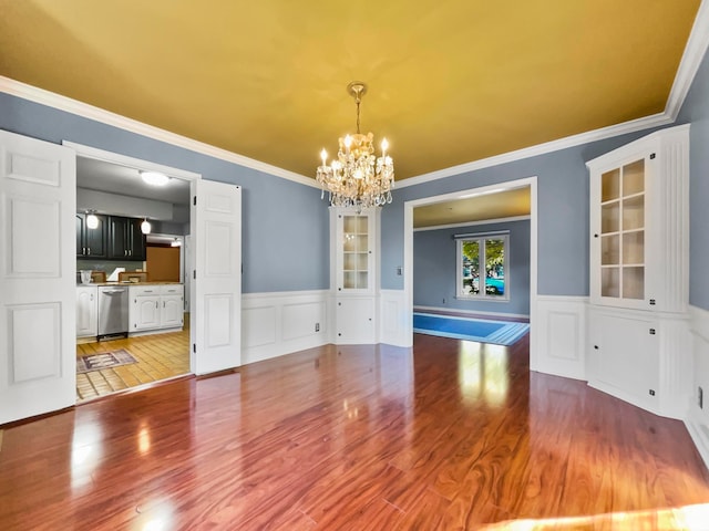 unfurnished dining area with an inviting chandelier, crown molding, and hardwood / wood-style floors