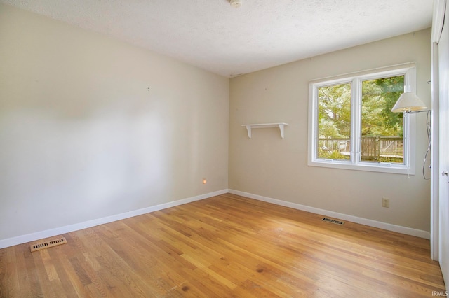 spare room featuring a textured ceiling and light hardwood / wood-style floors