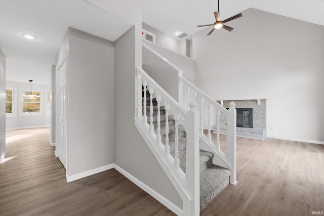 staircase featuring a brick fireplace, wood-type flooring, and high vaulted ceiling