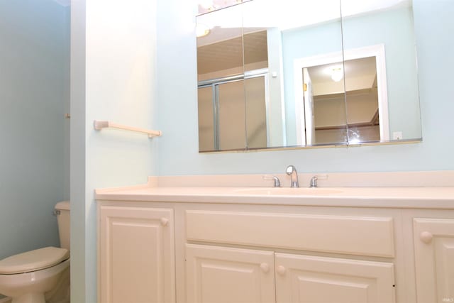 bathroom featuring a shower with door, vanity, and toilet