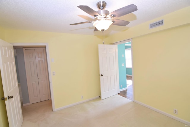 unfurnished bedroom featuring light carpet, a textured ceiling, a closet, and ceiling fan