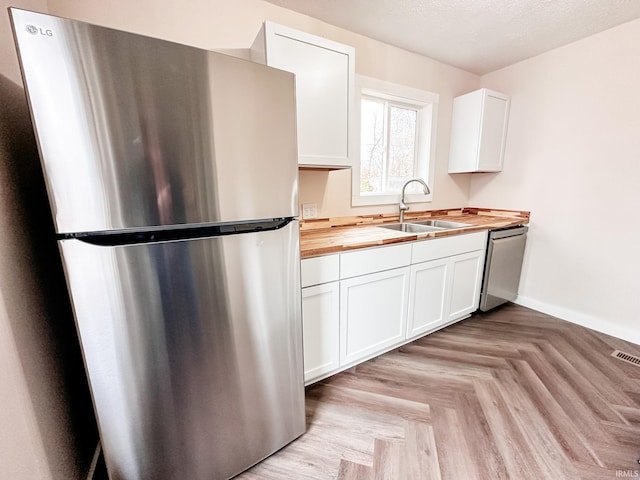 kitchen with stainless steel appliances, wood counters, sink, and white cabinets