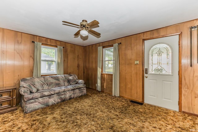 carpeted living room with ceiling fan and wood walls