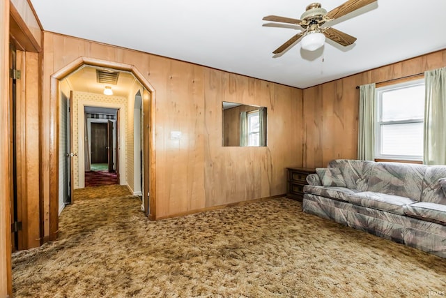 unfurnished living room with wooden walls, carpet floors, and ceiling fan