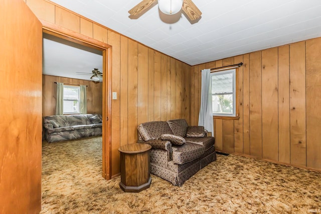 sitting room with ceiling fan, carpet flooring, and wood walls