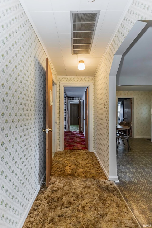 hallway with ornamental molding and dark colored carpet