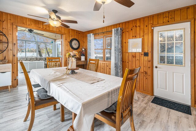 dining space featuring wooden walls, light hardwood / wood-style flooring, a textured ceiling, and ceiling fan