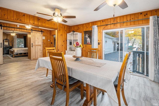 dining space featuring wooden walls, a barn door, and light wood-type flooring