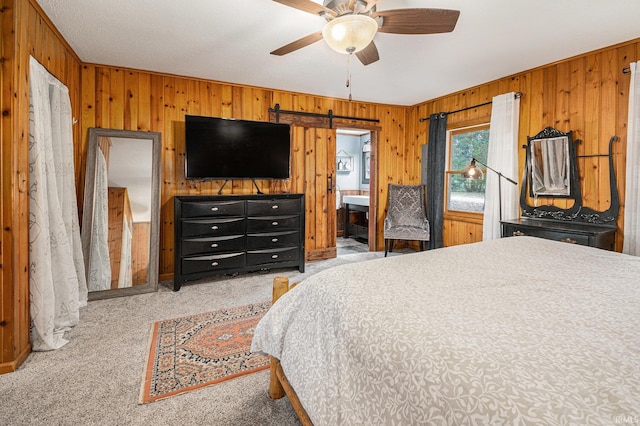 bedroom featuring ensuite bathroom, a barn door, ceiling fan, wooden walls, and light colored carpet