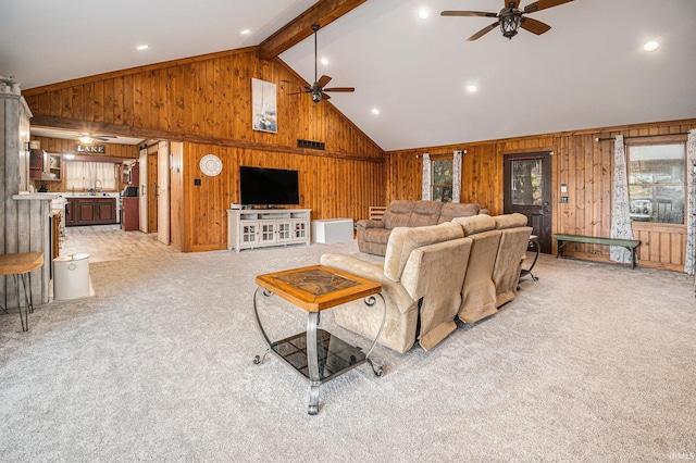 living room featuring beam ceiling, light carpet, ceiling fan, and wood walls