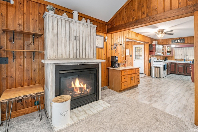 carpeted living room with wood walls, sink, a fireplace, ceiling fan, and lofted ceiling