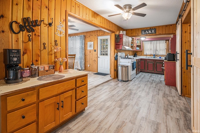 kitchen with stainless steel range with gas stovetop, light wood-type flooring, and wood walls