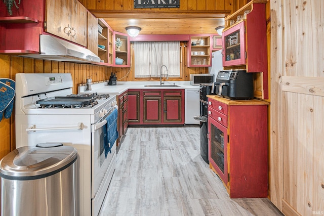 kitchen with white appliances, light hardwood / wood-style flooring, sink, and wooden walls