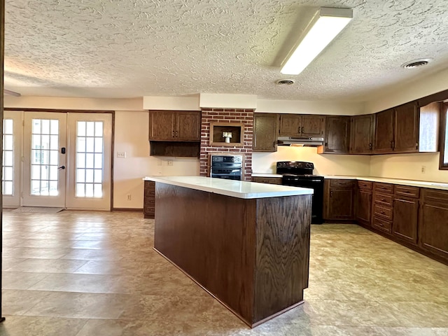 kitchen with dark brown cabinets, black appliances, a textured ceiling, and a center island