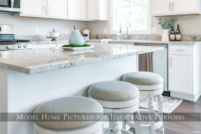 kitchen featuring light stone countertops, stainless steel appliances, wood-type flooring, and white cabinets