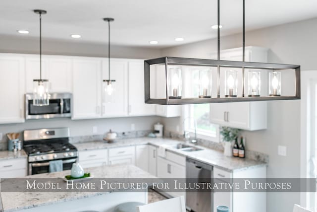 kitchen featuring light stone counters, appliances with stainless steel finishes, white cabinetry, sink, and decorative light fixtures