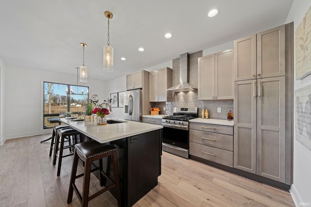 kitchen with wall chimney exhaust hood, appliances with stainless steel finishes, light hardwood / wood-style flooring, and an island with sink