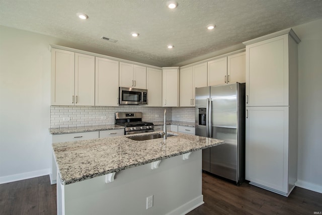 kitchen featuring dark wood-type flooring, an island with sink, stainless steel appliances, and white cabinetry