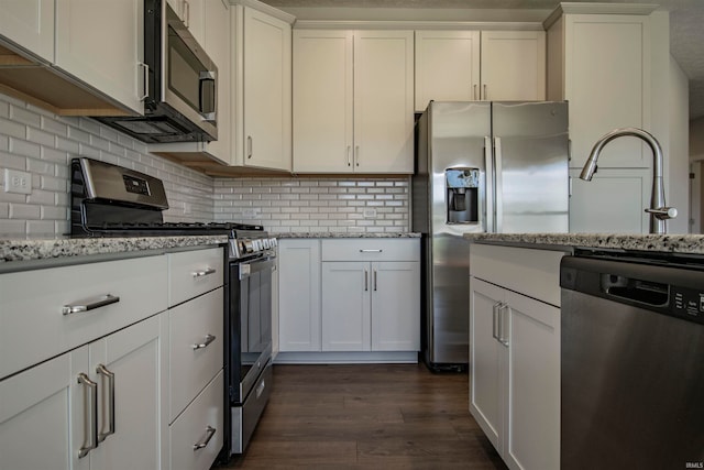 kitchen featuring white cabinetry, light stone counters, appliances with stainless steel finishes, and dark hardwood / wood-style floors