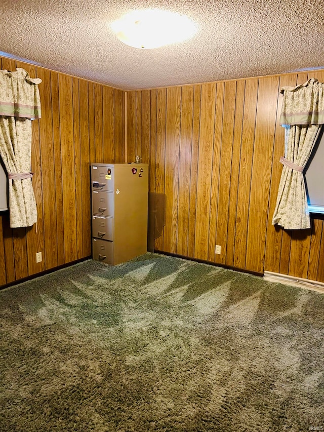 carpeted spare room featuring wooden walls, a baseboard heating unit, and a textured ceiling