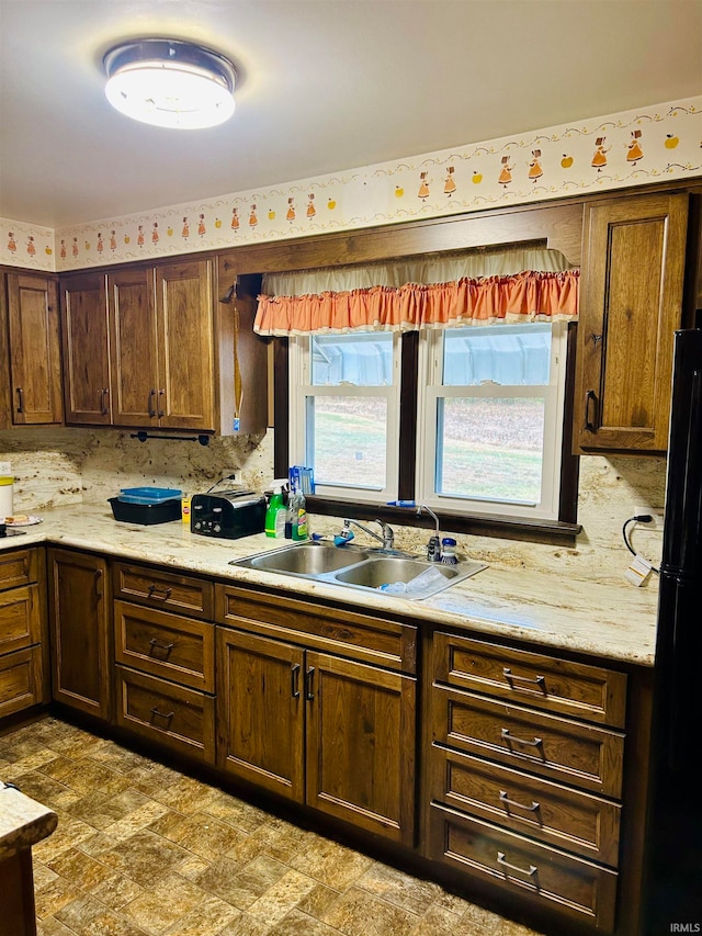 kitchen featuring light stone countertops, decorative backsplash, sink, and black fridge