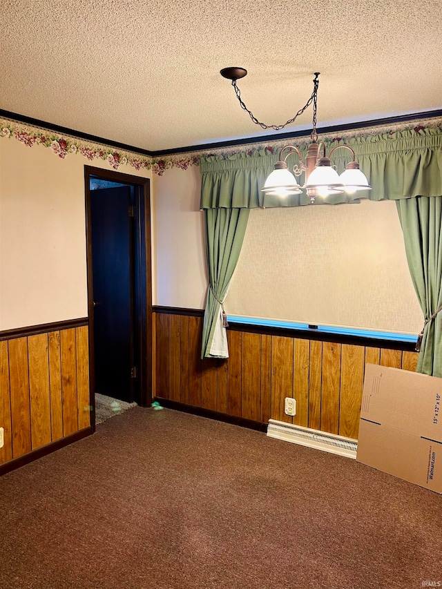 spare room featuring a baseboard radiator, wood walls, a textured ceiling, and carpet floors