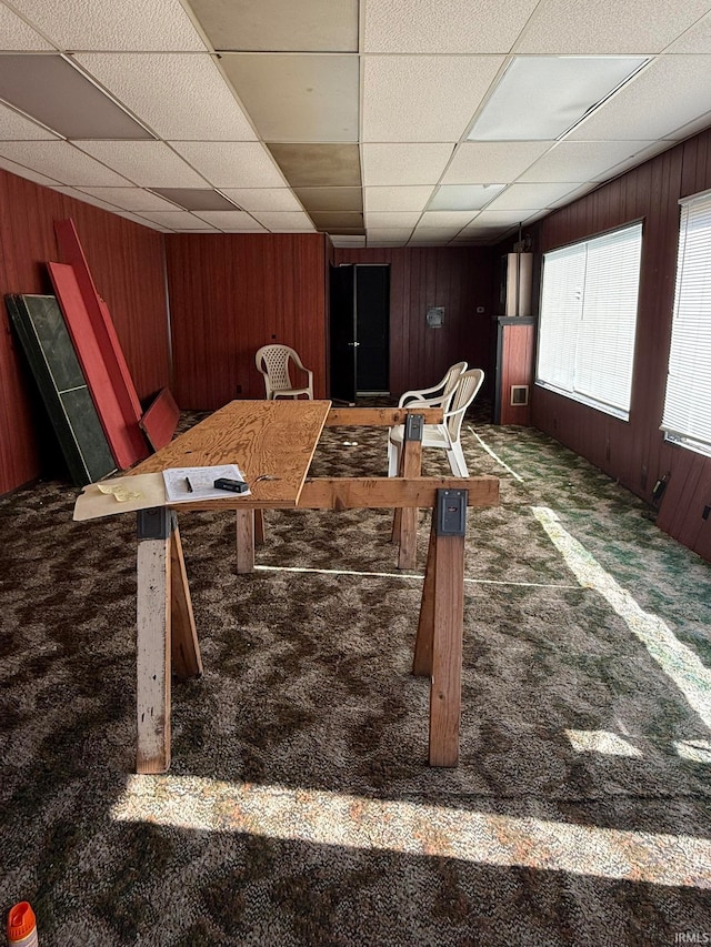 interior space with dark carpet, wooden walls, and a paneled ceiling