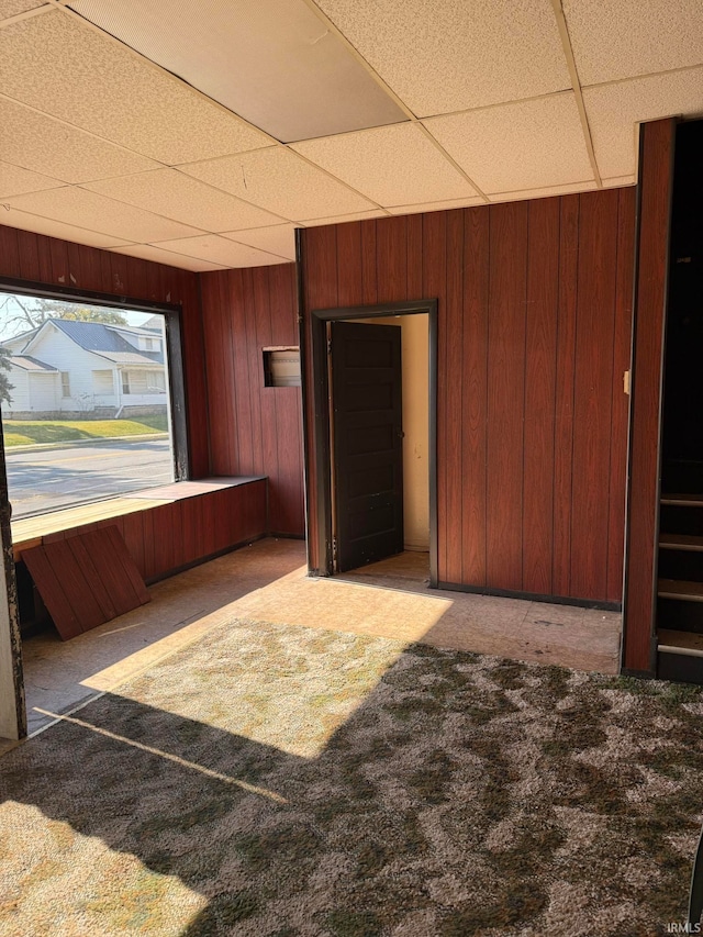 unfurnished room with dark carpet, wooden walls, and a drop ceiling