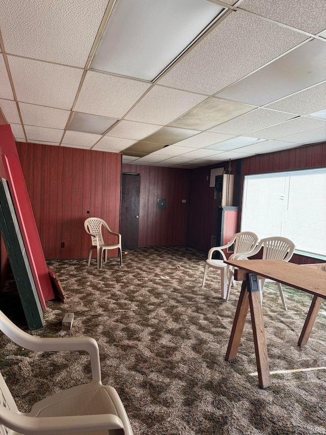 interior space featuring wood walls, a paneled ceiling, and dark colored carpet