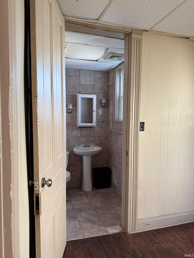 bathroom with toilet, wood-type flooring, sink, and a paneled ceiling