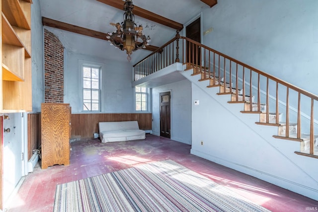 unfurnished living room with beam ceiling, an inviting chandelier, high vaulted ceiling, and wooden walls