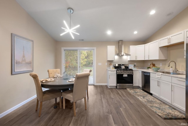 kitchen with wall chimney range hood, white cabinetry, stainless steel appliances, vaulted ceiling, and decorative light fixtures